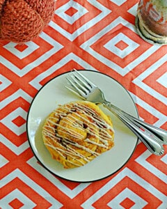 A close up of a cinnamon roll on a plate with glaze drizzled on top.