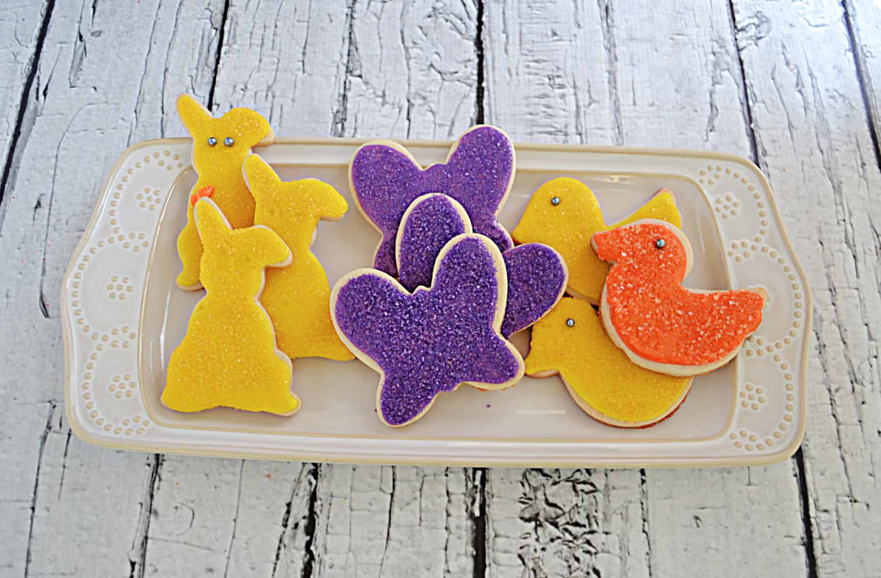 A platter with yellow bunny cookies, purple butterfly cookies, and orange bird cookies on it. 