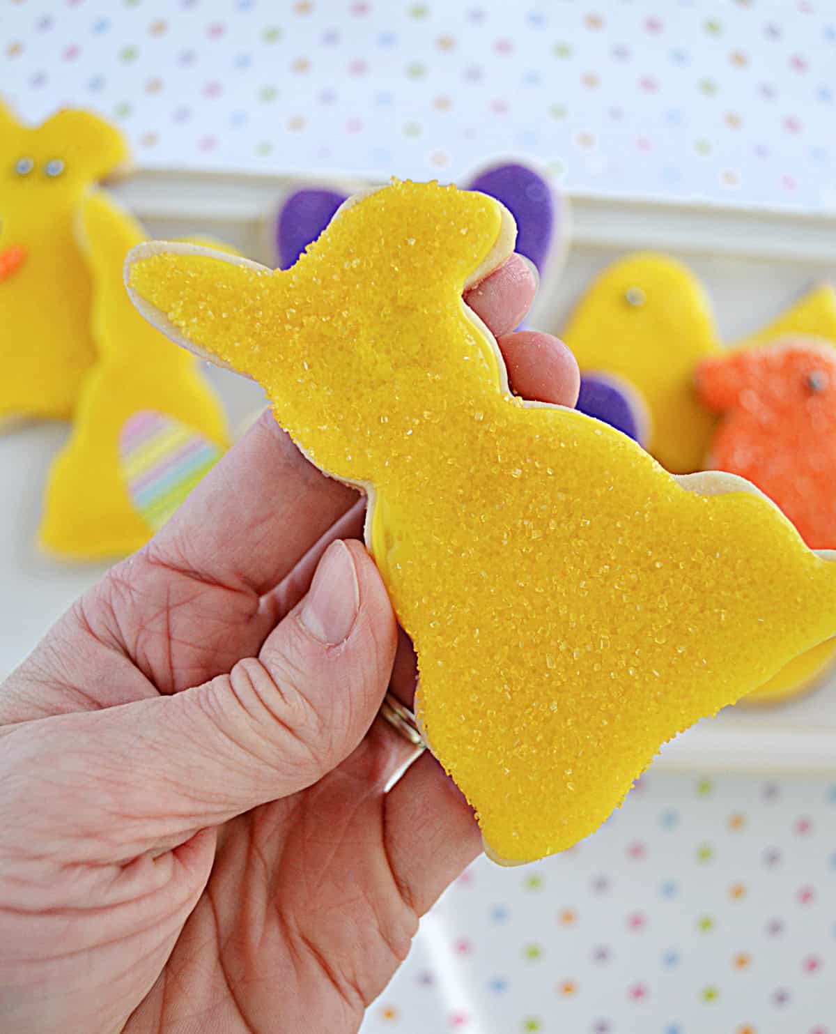 A hand holding a bunny sugar cookie with yellow icing and sugar on it.