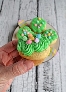 A hand holding a cookie with green frosting and egg sprinkles on it.