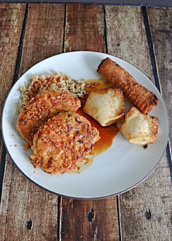 A plate with 2 pork chops in a soy glaze with 2 wontons and an egg roll.