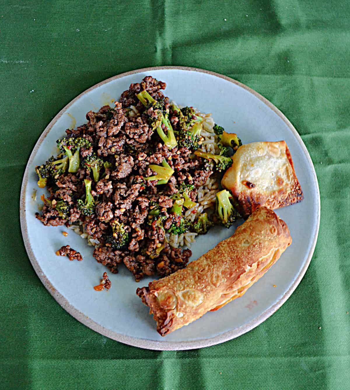 A plate with ground beef and broccoli, an egg roll, and a wonton. 
