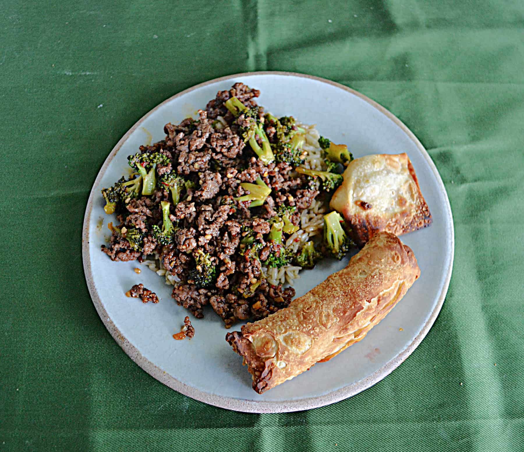 A plate of Korean Beef and Broccoli with an egg roll.