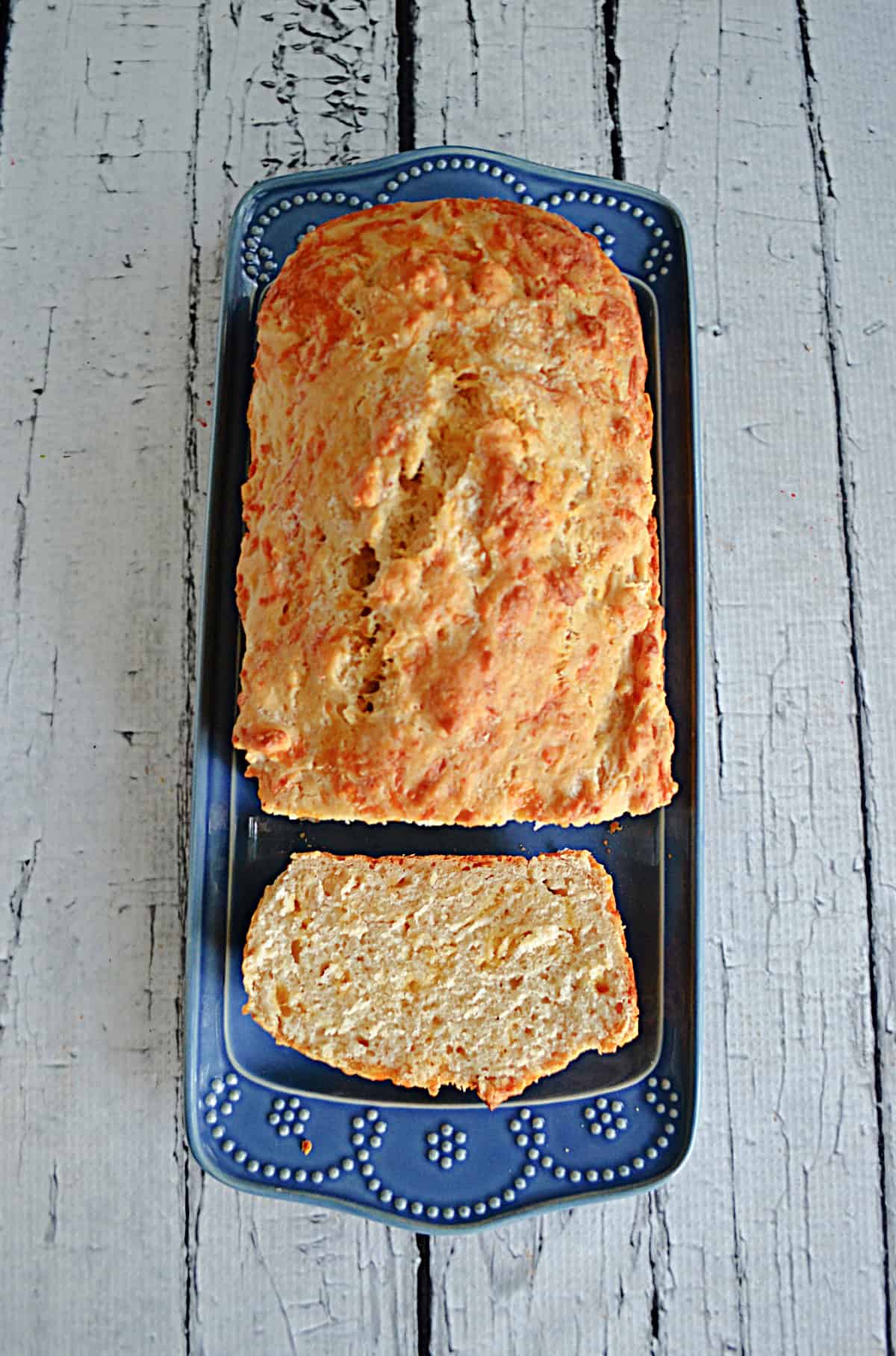 A loaf of Cheddar Beer Bread on a platter with a slice cut off.