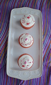 A platter with three pink velvet cupcakes on it.