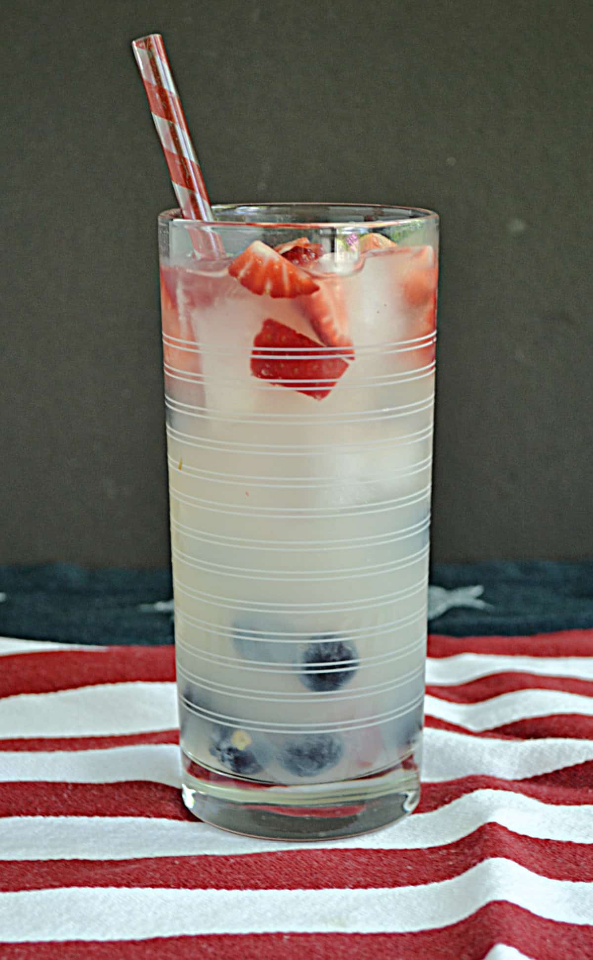 A glass of lemonade with red strawberries and blueberries in it. 