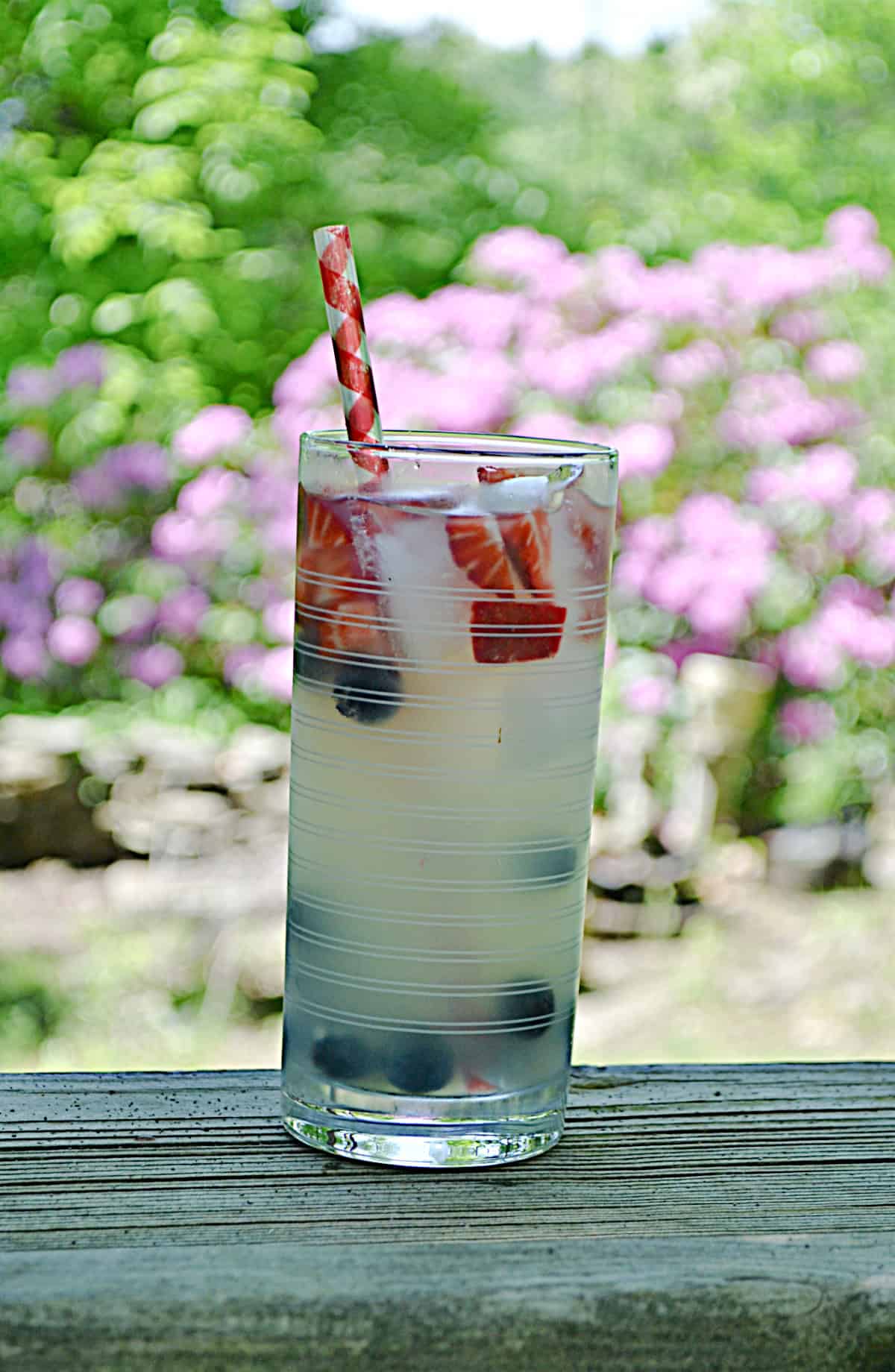 A tall glass of lemonade with red strawberries on top and blueberries at the bottom. 
