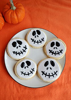 A plate of Jack Skellington cookies with pumpkins behind it.