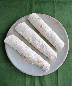 A plate with three wrapped tortillas on it.