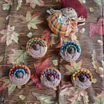 Five turkey cupcakes with a scarecrow behind them.