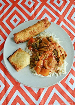 A plate of sesame chicken over rice with an egg roll,