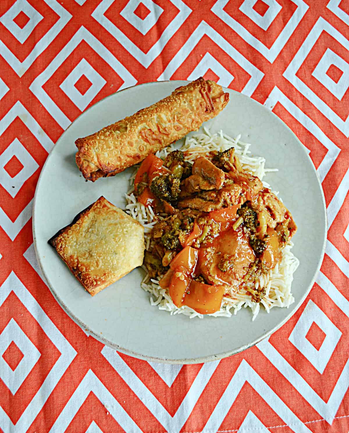 A plate of sesame chicken over rice with an egg roll,