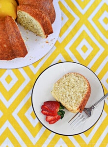 A slice of lemon Bundt cake laying on a plate with the whole cake in the background.