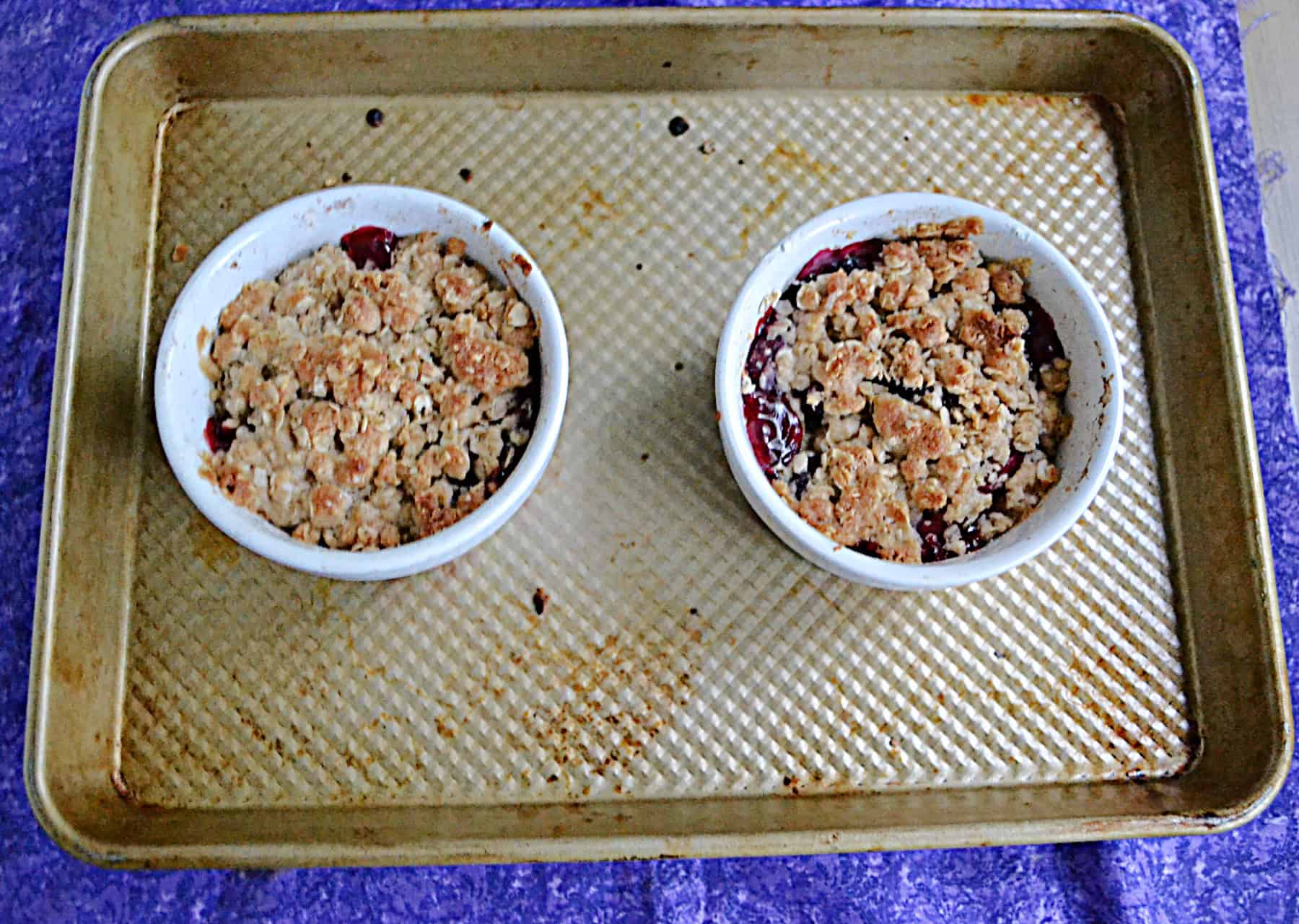 Two dishes of golden brown topped plum crisp.