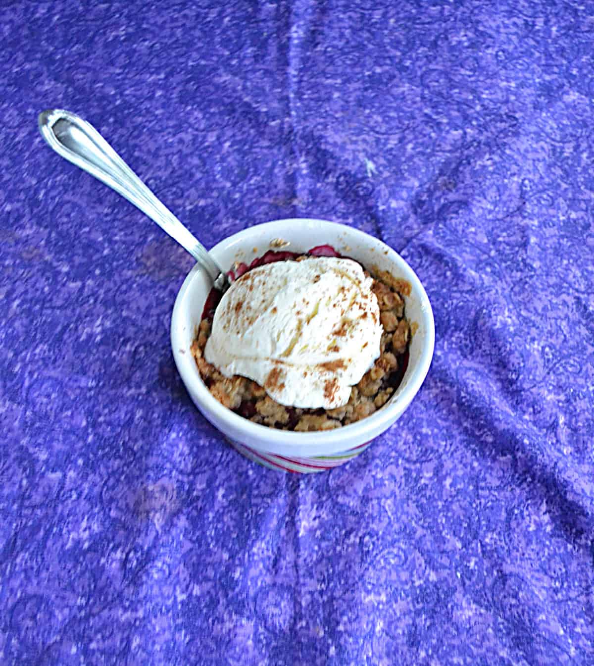 A ramekin with plum crisp topped with vanilla ice cream and a spoon in it.