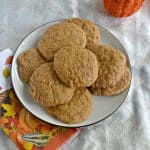 A white plate piled high with snickerdoodle cookies on top of an orange napkin with leaves on it and part of a pumpkin peeking in from the upper right hand corner.