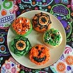 A plate with 5 orange and green Halloween Monster Donuts on it.
