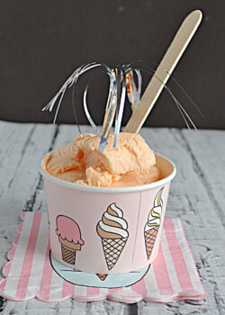 A cup of Thai Tea Ice Cream with a wooden spoon and silver streamer on top.