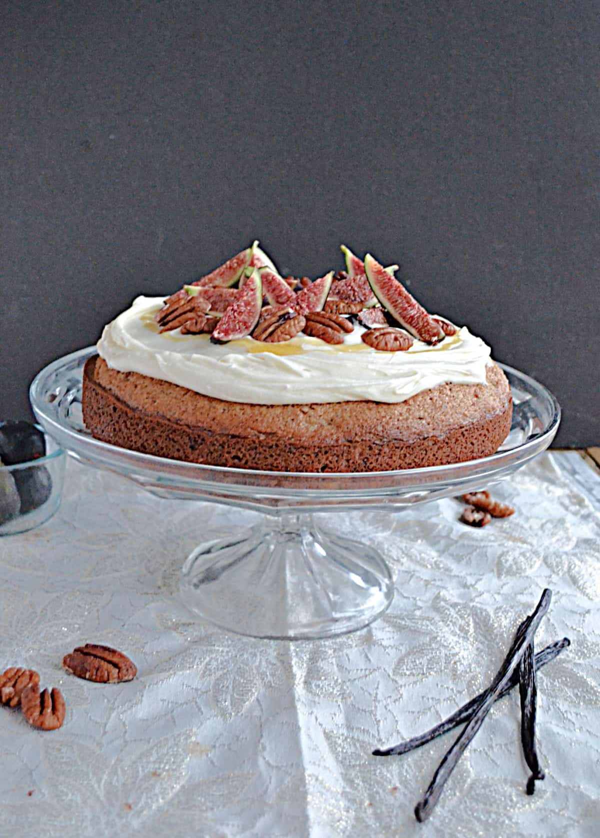 A cake on a cake stand topped with cream cheese frosting and fresh figs.
