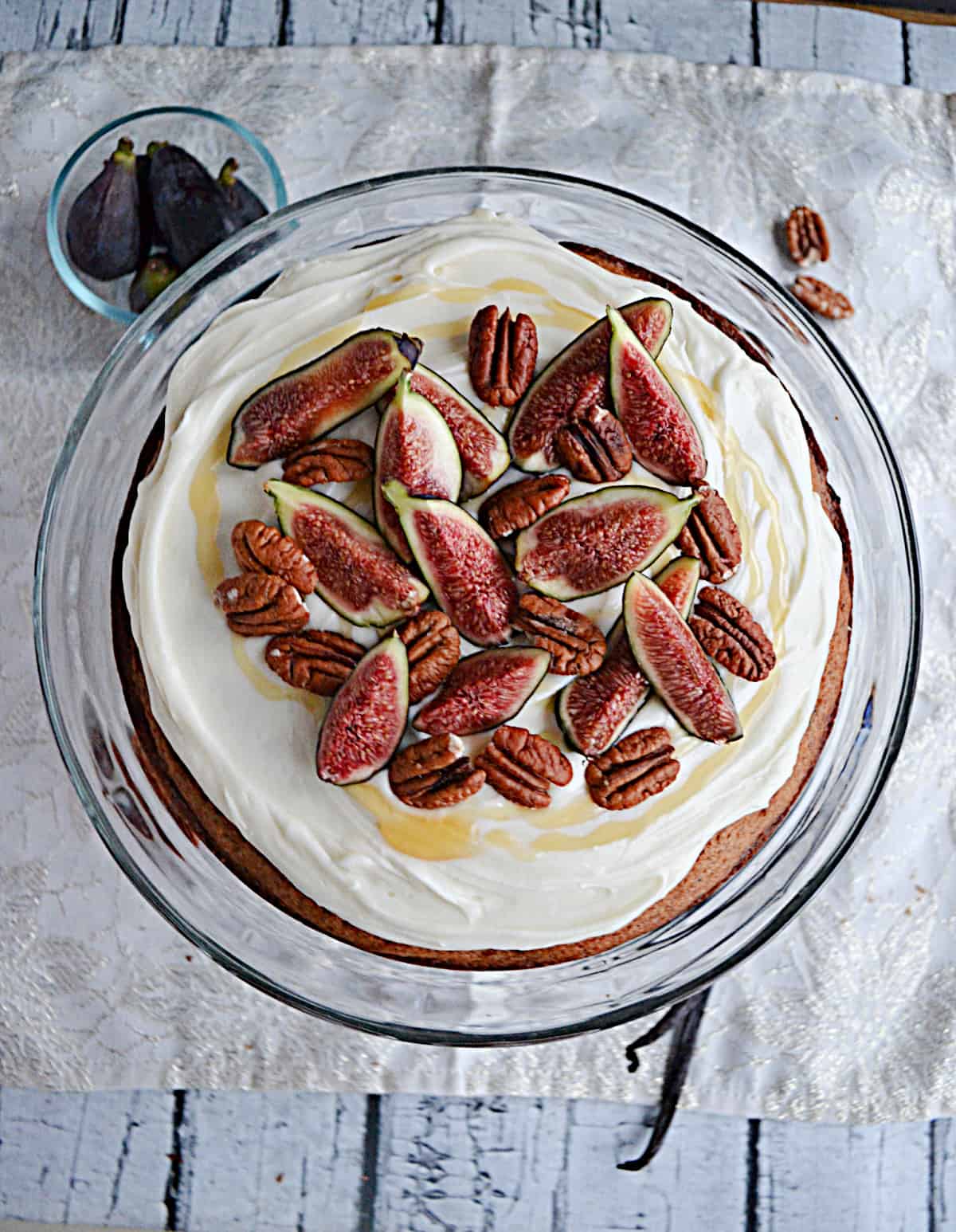 A top view of a cake with white frosting, fresh figs, honey, and pecans on top. 