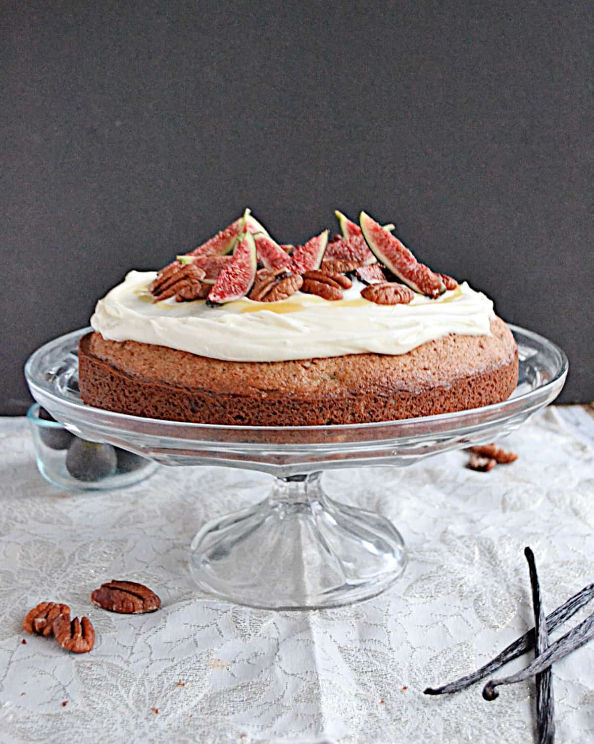 Front view of a cake on a cake stand with frosting, figs, and pecans on top. 