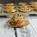A Chocolate Chip Zucchini Muffin sitting in front of a pan of zucchini muffins.