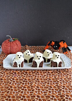 A platter with ghost brownies on it and a pumpkin and spider behind the platter.