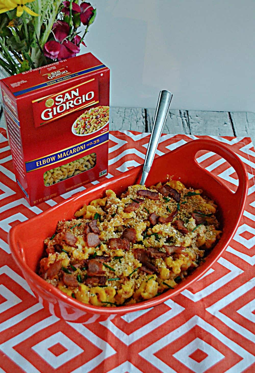 A baking dish of macaroni and cheese with a box of macaroni behind it.