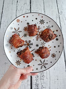 A hand holding a plate of bacon wrapped meatballs.