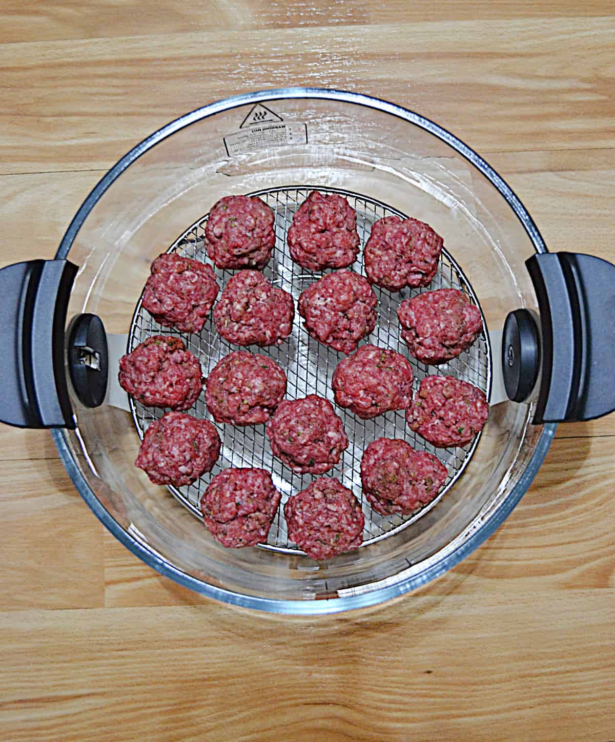 A bunch of meatballs in the bowl of the air fryer ready to be cooked.