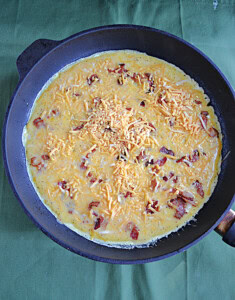 A skillet with eggs and bacon and cheese on top.