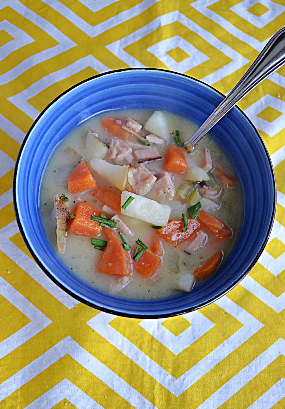 A bowl of soup with carrots, ham, and potatoes with a spoon in it.