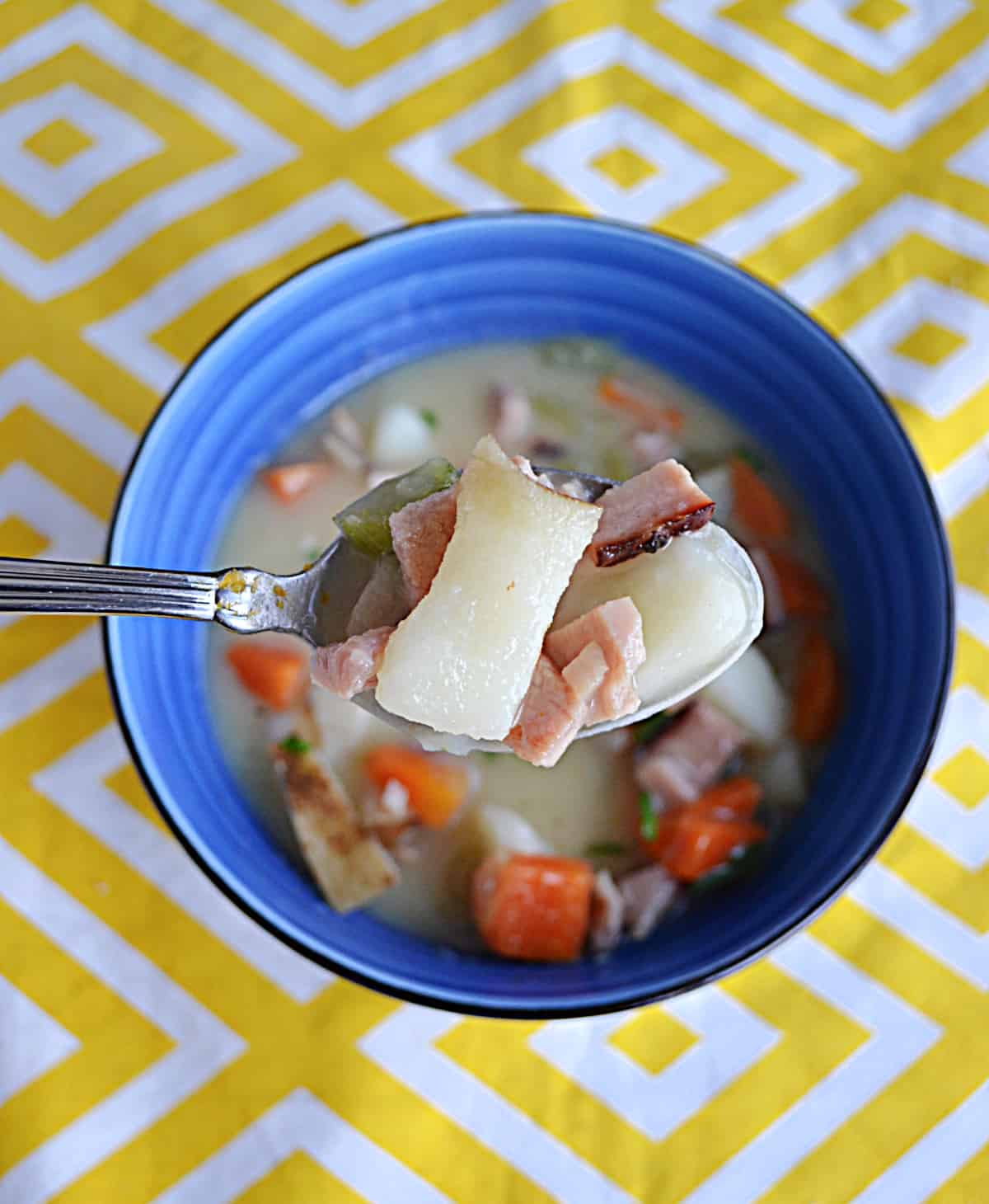 A spoon holding potatoes, ham, carrots, and soup broth on a spoon.