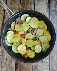 A skillet with zucchini, squash, and bacon in it.