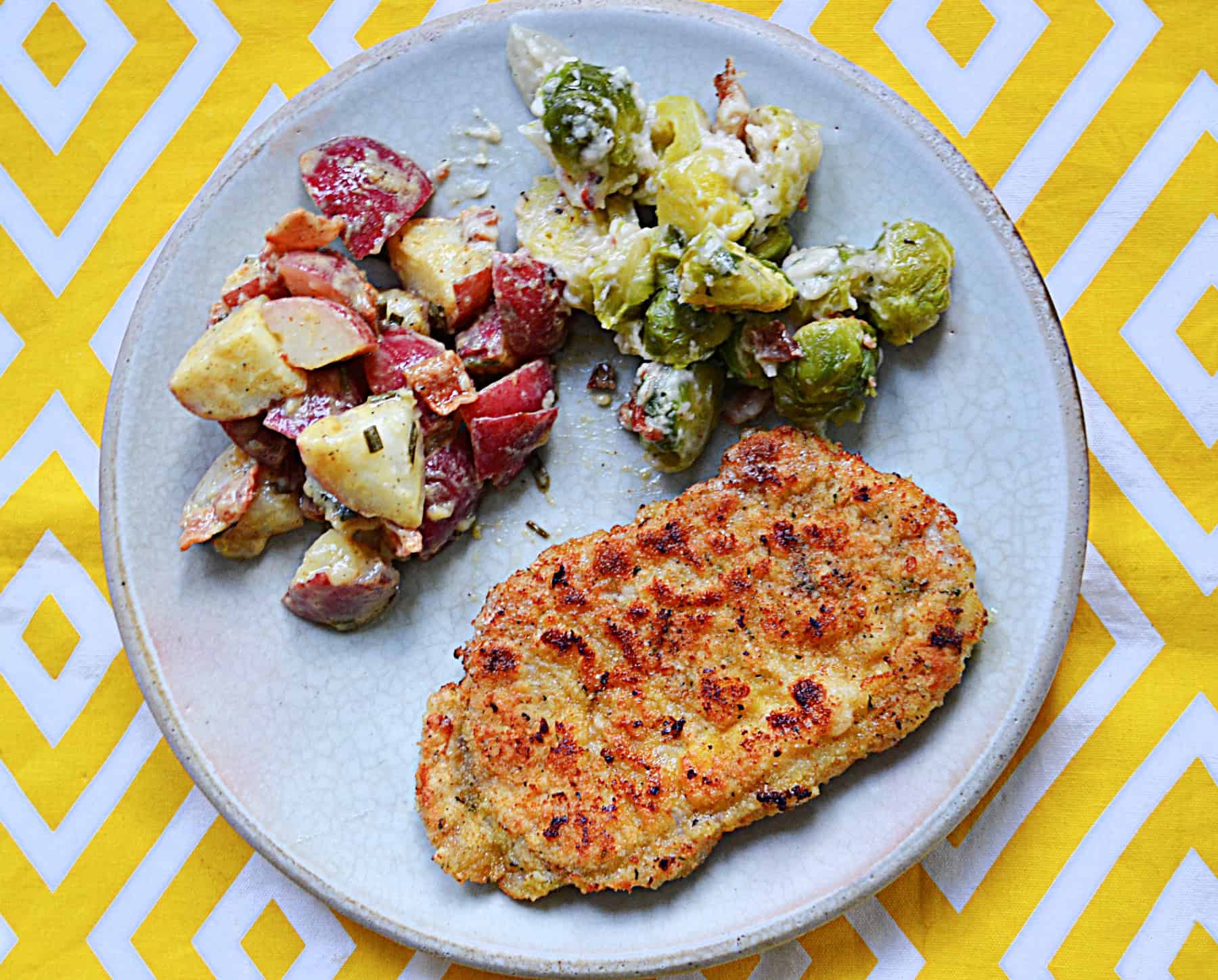 A plate of pork schnitzel, German potato salad, and Brussels Sprouts.