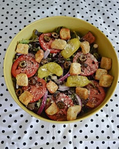 A bowl of salad with croutons, tomatoes, and pepperoncinis on top.