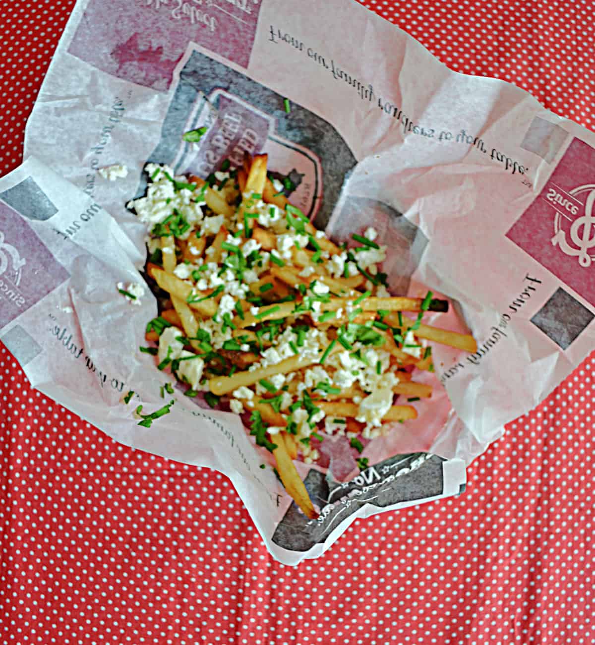 A basket of fries with herbs and feta cheese on top.
