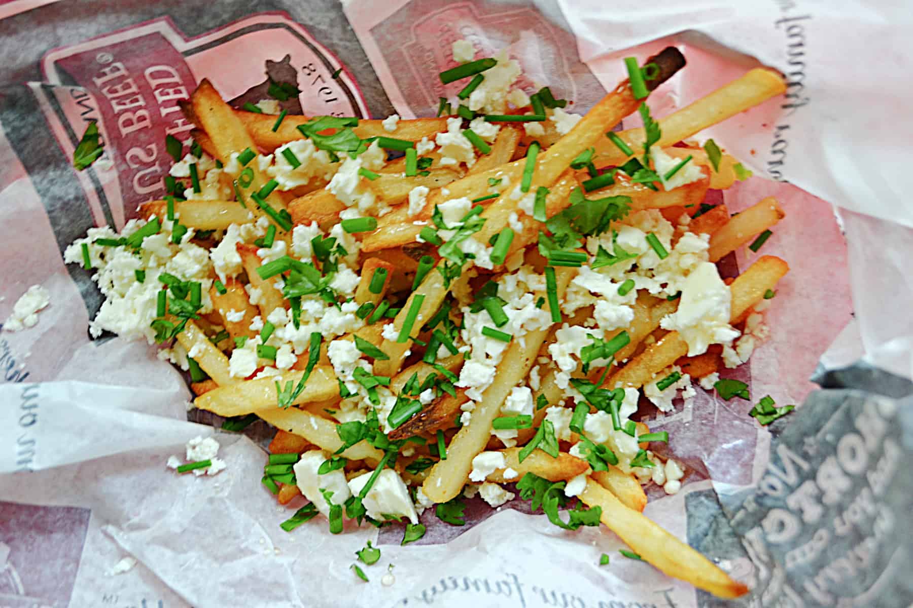 A close up of a pile of french fries with herbs and feta on top.