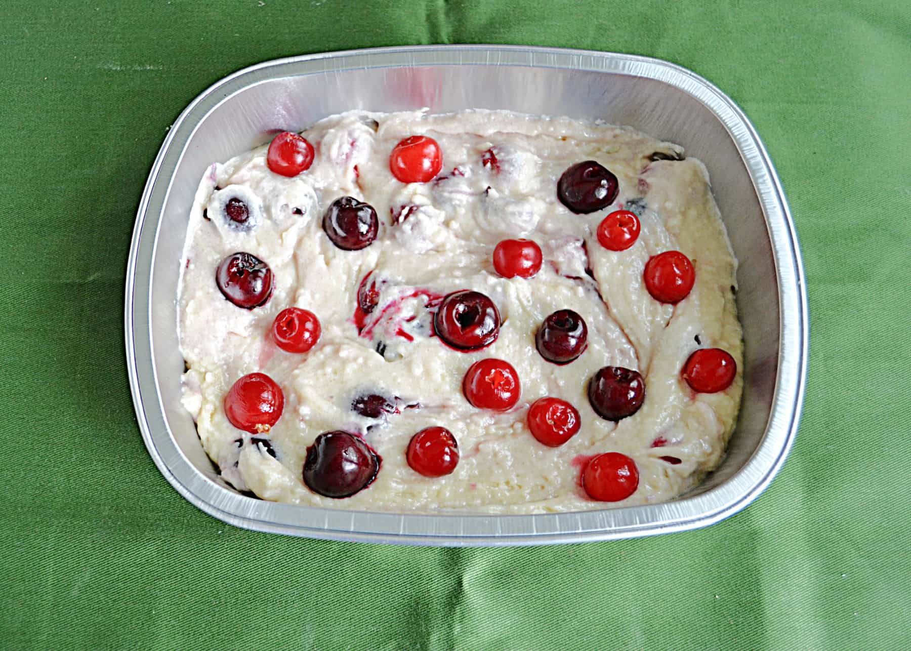 A pan of batter with fresh cherries on top.