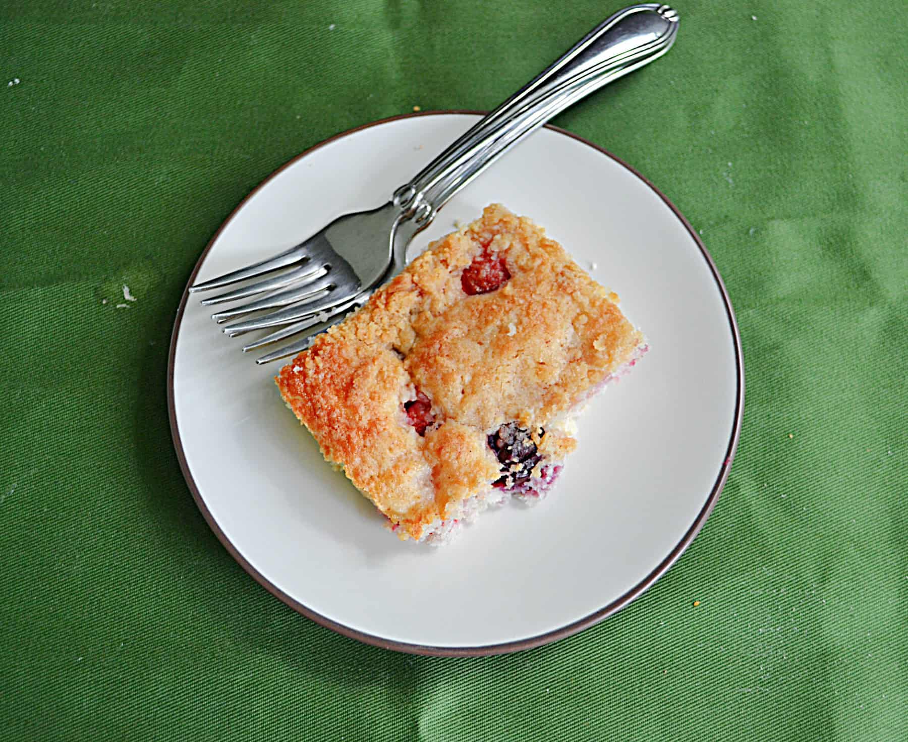 A plate with a piece of cherry coffee cake and a fork on it.