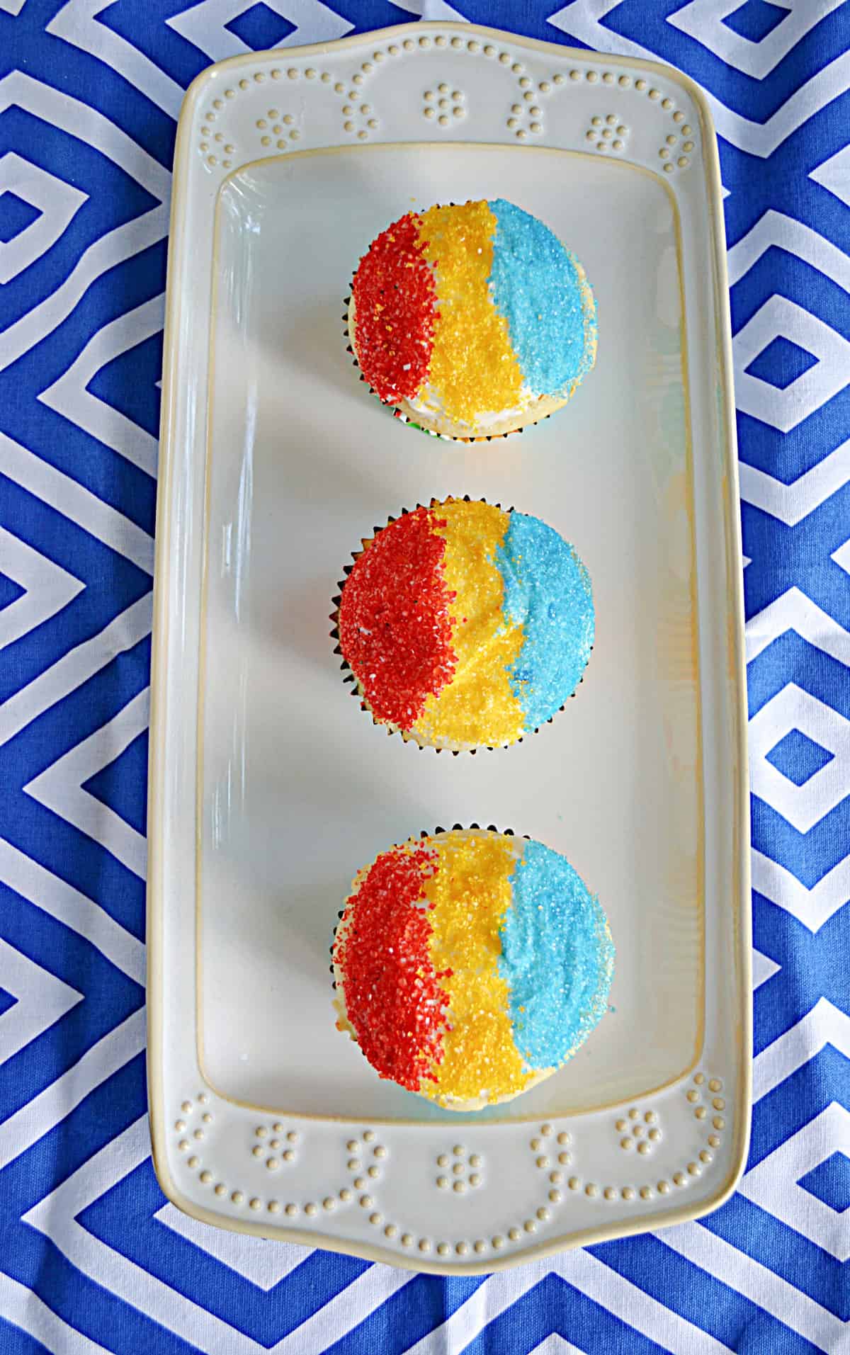 A platter of 3 Snow Cone Cupcakes with red, yellow, and blue sanding sugar.