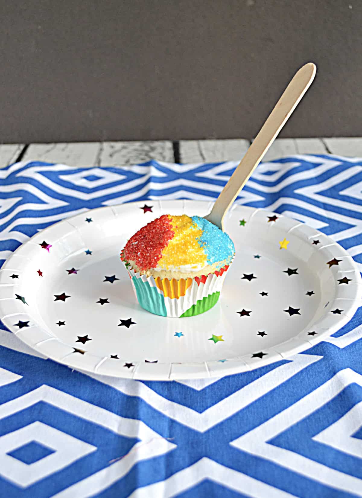 A snow cone cupcake on a plate with a wooden ice cream spoon in it.