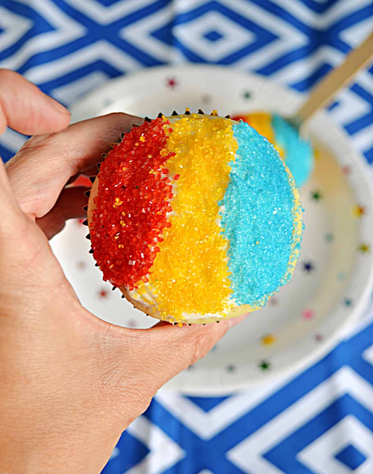 A close up view of a snow cone cupcakes with red, yellow, and blue sanding sugar.