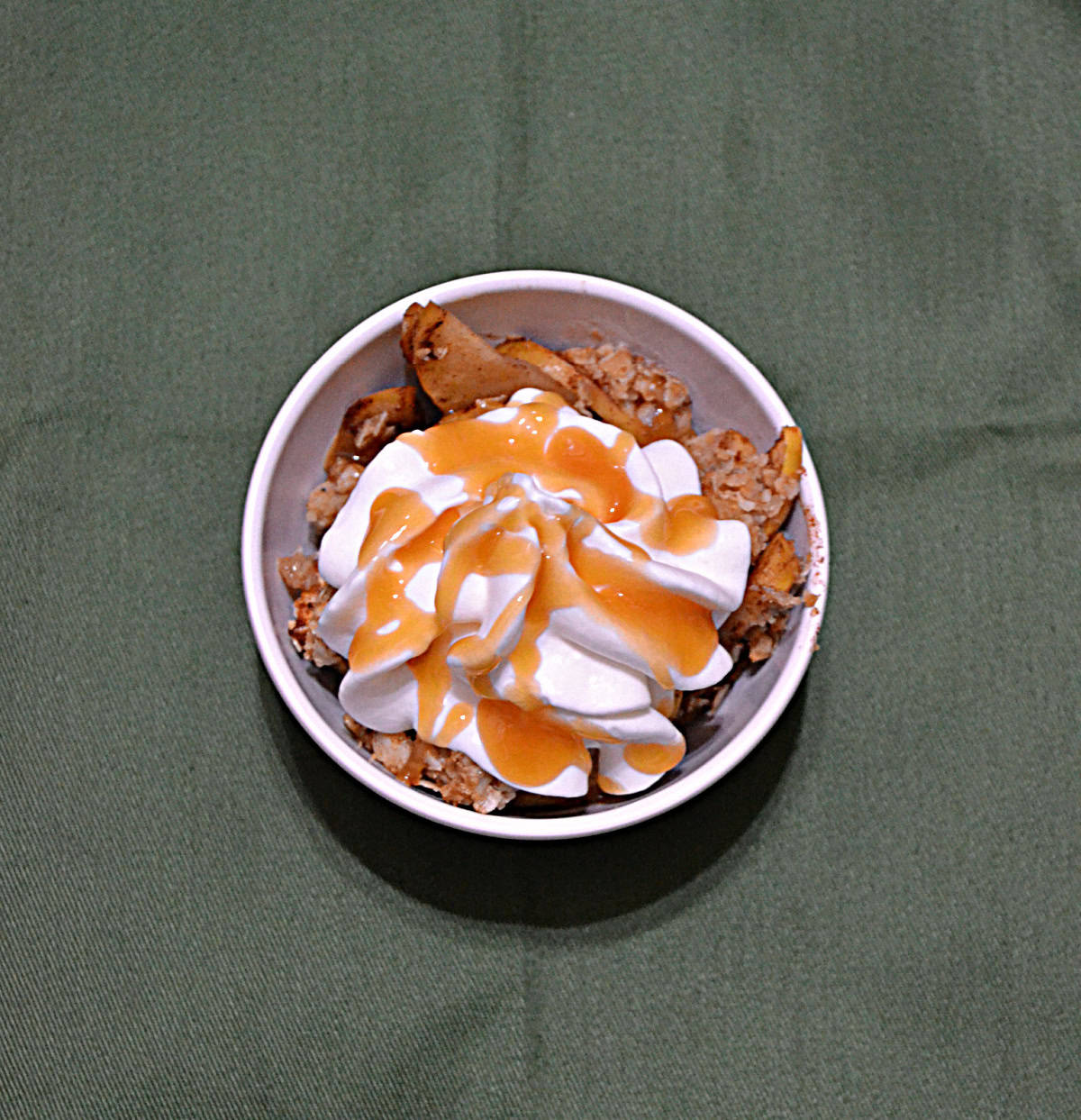 A bowl of apple crisp topped with whipped cream and caramel sauce.