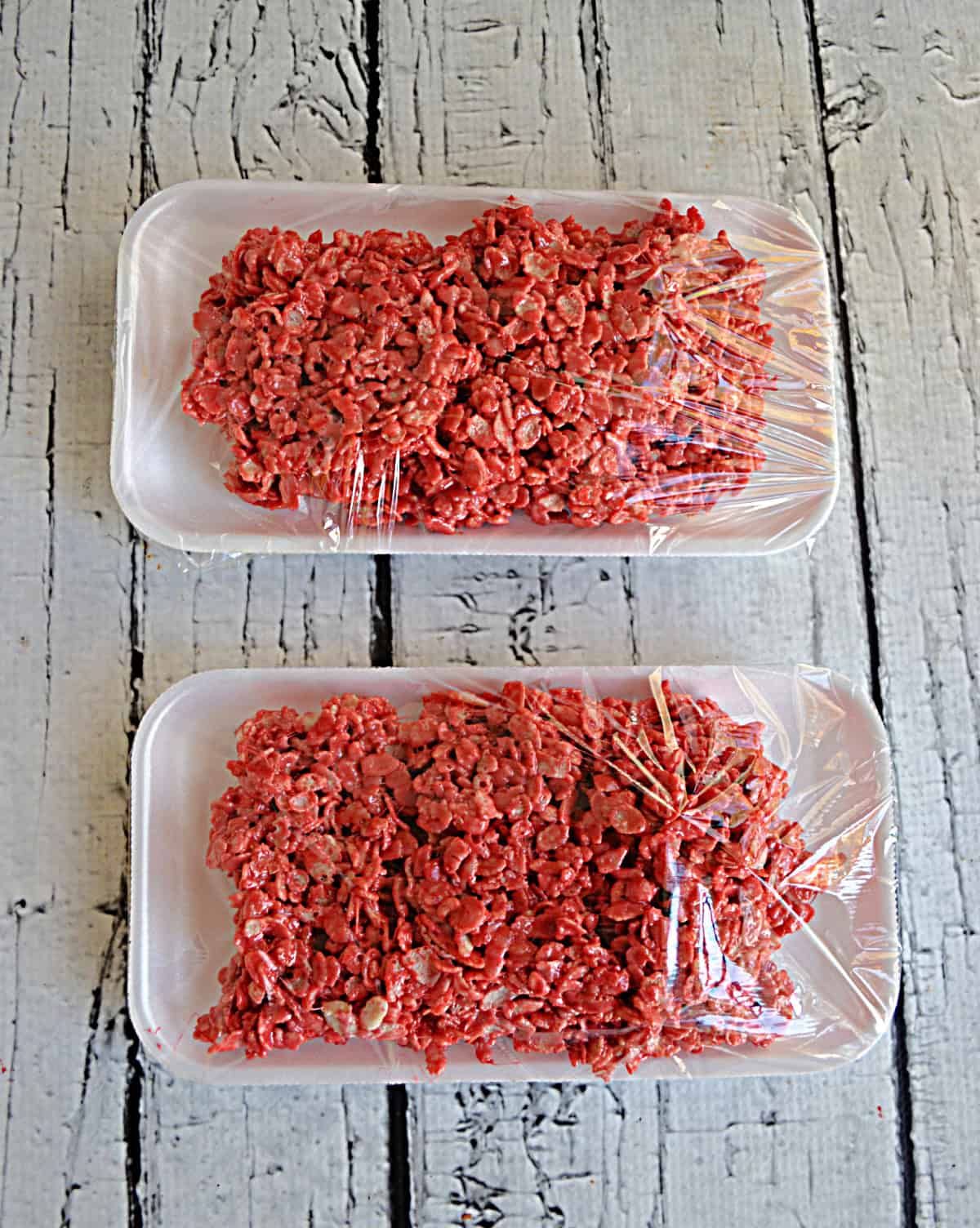 Two trays filled with red Rice Krispies Treats covered in plastic wrap.