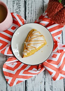 A plate with a glazed pumpkin scone on it.